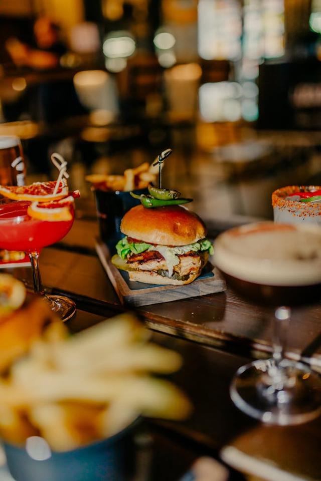 A chicken burger next to cocktails and chips on the table.