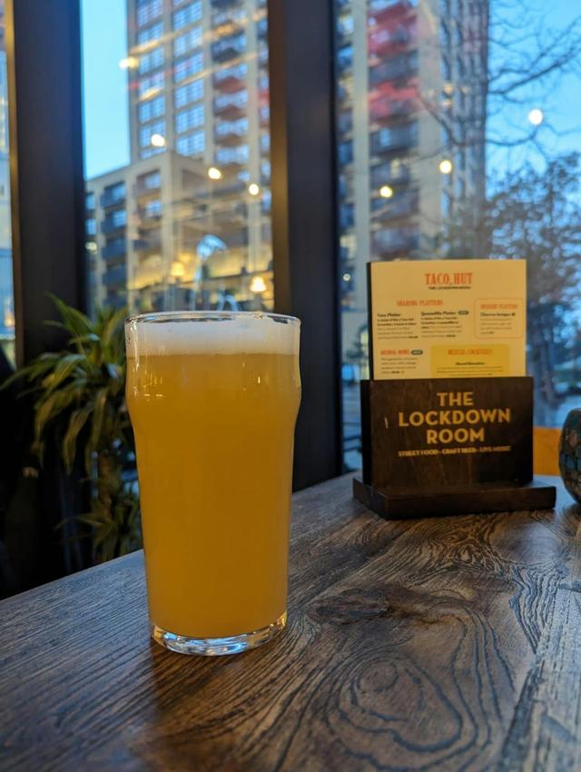 Picture of a pint of pale ale on an oak table with the Lockdown Room menu by its side. Buildings in the background